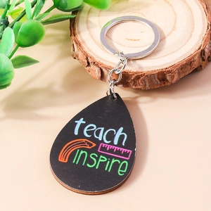 Close-up of wooden teardrop keychain with teach inspire lettering and school motifs
