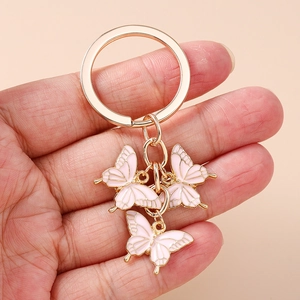 Main tenant un porte-clés papillon rose élégant avec des charms en émail et doré