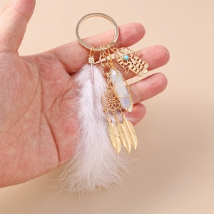 Detail of bohemian gold keychain with white feather, Hamsa hand, and dreamcatcher charms