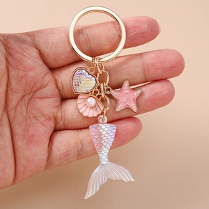 Fashionable mermaid tail keychain with heart shell charms on gold ring held in hand