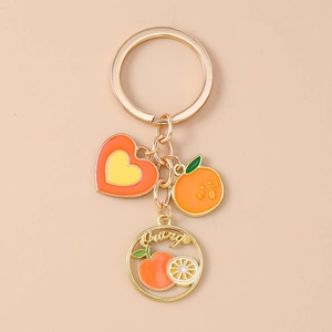 Close-up of golden fruit keychain featuring orange heart, small orange, and metal orange text