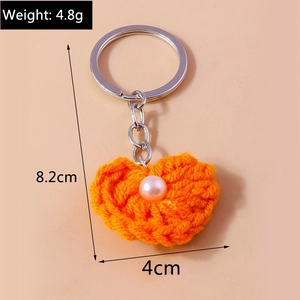 Detail von handgefertigtem orangefarbenem Strickherz-Schlüsselanhänger mit Perle und Ring