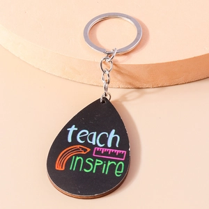 Detail of teardrop wooden keychain featuring Teach Inspire text and school motifs