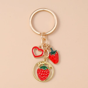 Close-up of strawberry keychain with red heart charm and engraved gold medal