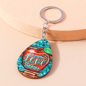Close-up of wooden teardrop keychain with red apple design and Teach Love Inspire text