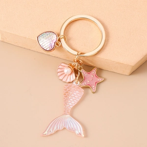 Detail of pink gradient mermaid tail keychain with heart shell and golden ring accessories