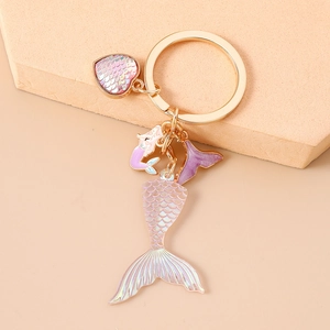 Close-up of heart charm and mermaid tail keychain with iridescent scales and gold finish