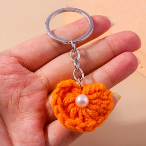 Detail eines handgestrickten orangefarbenen Herz-Schlüsselanhängers mit Perle und Ring