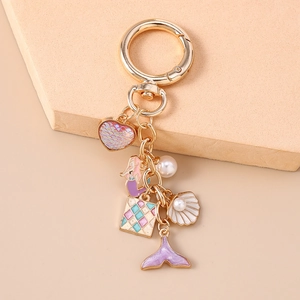 Detail of mermaid keychain with fish tail, shell charms and pearls on a peach display