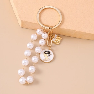 Detail of a gold keychain with pearls, an enamel lady profile, and a quilted bag charm