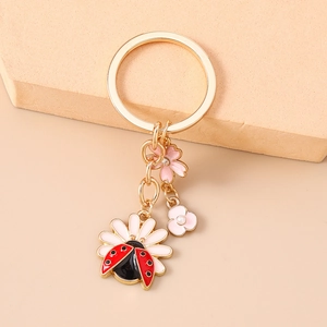 Detail of floral keychain with daisy ladybug charms and pink blossoms on golden ring