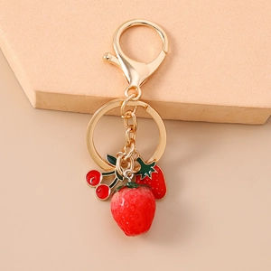 Macro shot of gold keychain with 3D strawberry and cherry charms on a warm background