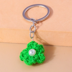 Close-up of handmade green knitted flower keychain with a pearl center and silver metal ring
