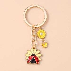 Detailed close-up of golden keychain featuring enamel daisy flowers and a ladybug charm