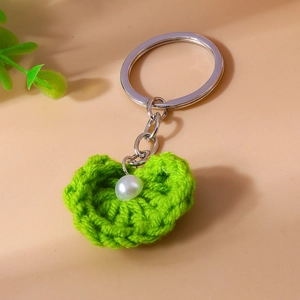 Detail eines grünen handgestrickten Herz-Schlüsselanhängers mit Perle und Ring