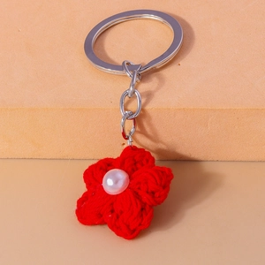 Detail of red crochet flower keychain with central white pearl and silver metal ring