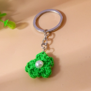 Close-up of green knitted flower keychain with white pearl center and silver ring