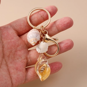 Detail of beach shell keychain with golden lobster clasp held against pink background