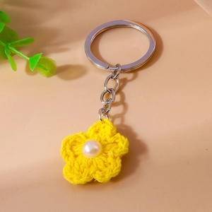 Detail of yellow knitted flower keychain with a white pearl center and silver metal ring