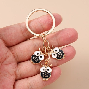 Gros plan d'un porte-clés doré avec trois pendentifs hiboux en émail noir et blanc