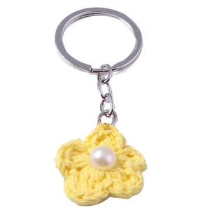 Close-up of handmade yellow crochet flower keychain with central white pearl and silver ring