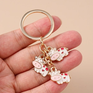Detail of three cartoon cow keychains with red hearts held in hand against a plain background
