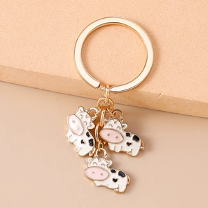 Detail of cute enamel cow pendants on a golden keychain with a warm beige background