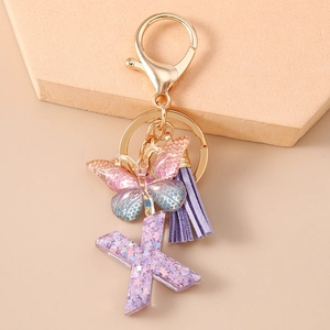 Dettaglio portachiavi con lettera X glitterata, nappa viola e ciondolo a farfalla