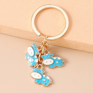Close-up of golden keychain with three blue and white enamel cartoon cow charms
