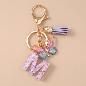 Dettaglio del portachiavi con lettera M, farfalla glitterata e nappa in pelle viola