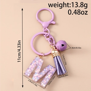 Détail du porte-clés lettre M violet avec paillettes en résine, pompon et cloche