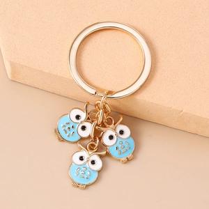 Vue détaillée du porte-clés doré avec trois pendentifs hiboux en émail bleu clair