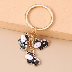 Detail of golden key ring with three cute black and white enamel cartoon cow pendants