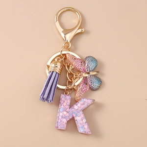 Dettaglio del portachiavi con nappa viola, farfalla e lettera K in resina con paillettes