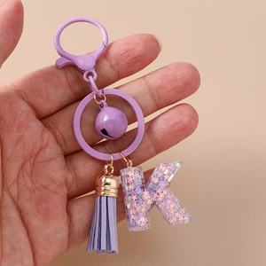Détail macro d'un porte-clés lettre K en résine violette avec paillettes et pompon