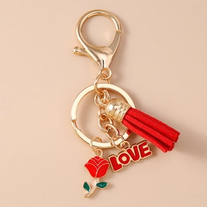 Detailansicht von roter Quaste, Rosenanhänger und LOVE-Anhänger an Gold-Schlüsselanhänger