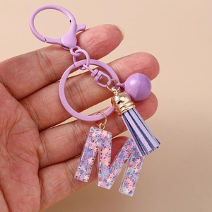Détail du porte-clés lettre M en résine violette avec paillettes et pompon en cuir
