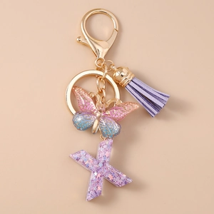 Dettaglio portachiavi con nappa viola, farfalla sfumata e lettera X in acrilico glitter