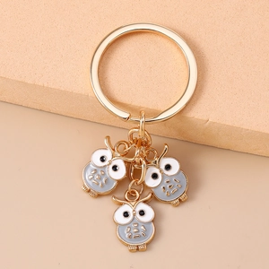 Détail d'un porte-clés doré avec trois pendentifs hiboux en émail gris et blanc