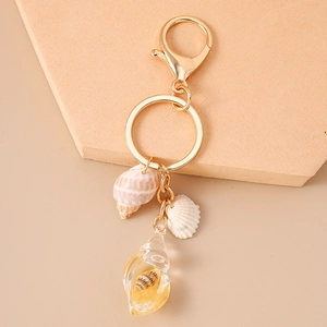 Close-up of golden keychain with natural shells and luminous conch resin pendant