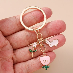 Detailed close-up of a golden keychain featuring pink enamel bunny, tulip and rose charms