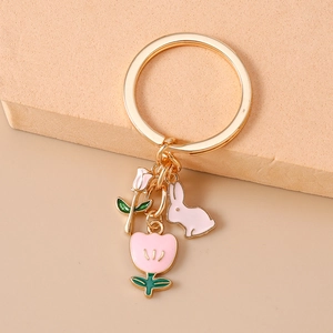 Detailed macro view of pink enamel tulip, rose, and bunny charms on a gold keychain