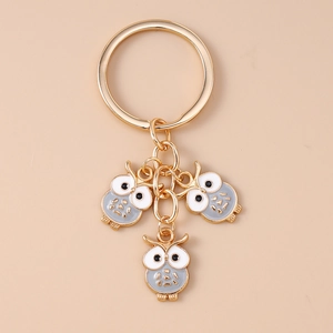 Vue détaillée de trois breloques chouettes en émail sur un porte-clés doré en métal poli