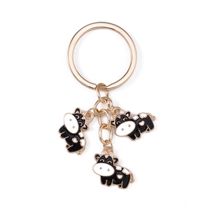 Golden keychain with cute black and white enamel cow pendants featuring heart patterns