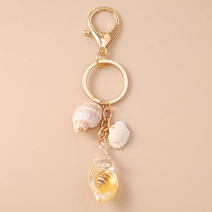 Detail of a golden beach shell keychain featuring a translucent conch pendant with gold flakes