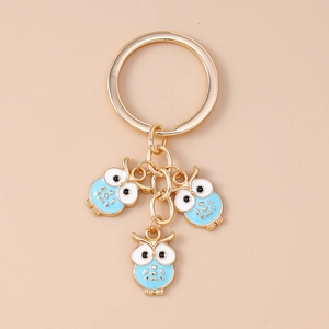 Détail d'un porte-clés doré avec trois pendentifs hiboux en émail bleu et blanc