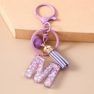 Détail de porte-clés lettre M en résine violette avec paillettes et pompon en daim