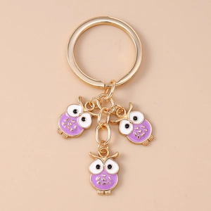 Détail d'un porte-clés doré avec trois pendentifs hiboux en émail violet et blanc