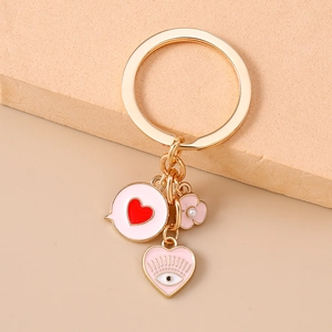 Detail of gold keychain with pink enamel heart, floral charm and evil eye pendant