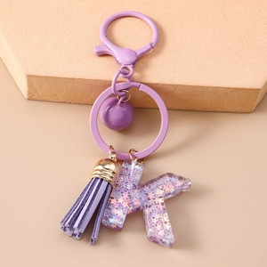 Détail du porte-clés lettre K en résine violette avec pompon et paillettes étincelantes